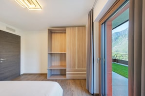Un dormitorio moderno con cama, estanterías empotradas de madera y puerta corredera de cristal que da a un balcón con vistas a la montaña.
