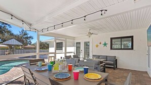 Un patio exterior con piscina, mesa de comedor, platos y vasos, y un ventilador de techo.