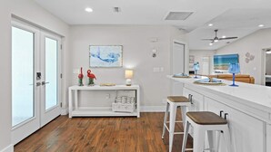 Una cocina moderna con armarios blancos, piso de madera y una barra con taburetes.