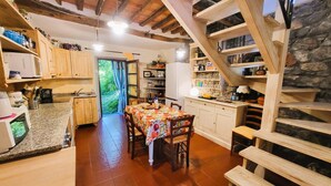 Eine rustikale Küche mit Holzausstattung, einem Esstisch mit Stühlen und einer Treppe mit Steinwand.