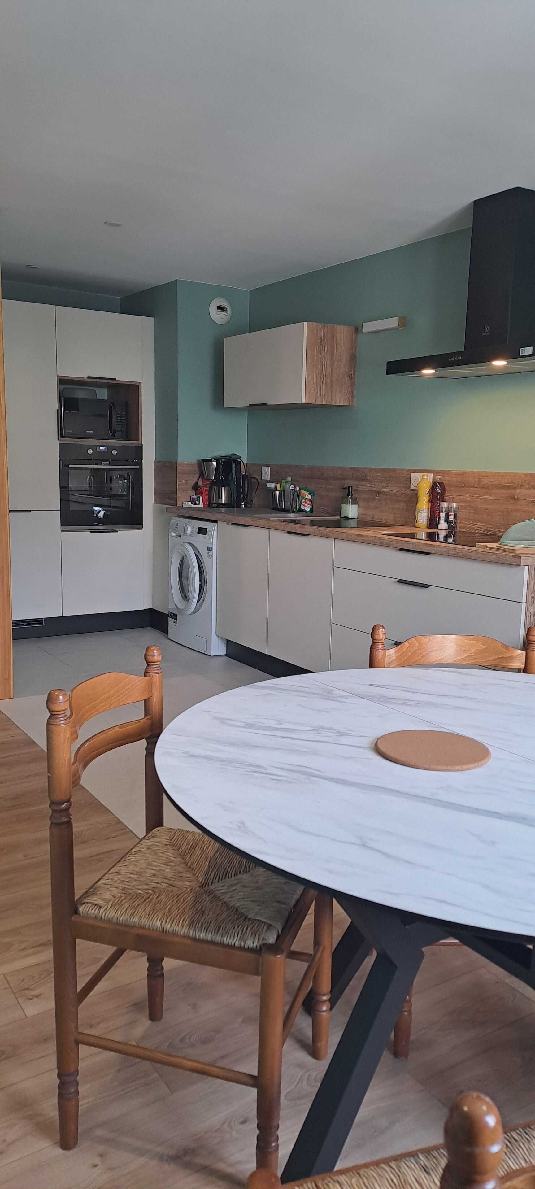 Une cuisine moderne dotée d’appareils électroménagers intégrés, une table à manger avec des chaises et un lave-linge.