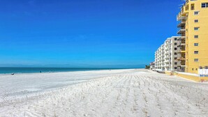 Una playa con cielo despejado, orilla arenosa y un edificio amarillo de varios pisos y balcones.