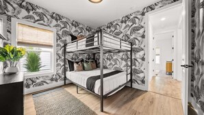 A room with a bunk bed, a desk with a plant, a window with blinds, and a door leading to another room. - Beach & Lake | Private Pool | Game Room | Near 30A (Panama City Beach)