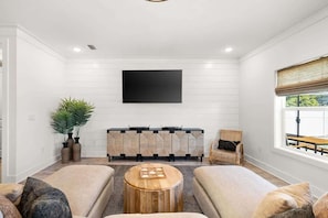 Ein Wohnzimmer mit flachbildfernseher an der Wand, einer Sofagarnitur, einem Couchtisch und einem Beistelltisch.