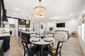 A modern kitchen with a central island, dining area with round table and chairs, and a living room with a sofa and television. - Beach & Lake | Private Pool | Game Room | Near 30A (Panama City Beach)