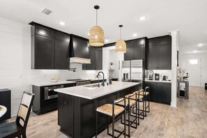 Une cuisine moderne avec des meubles de couleur sombre, un îlot central doté de tabourets et un éclairage suspendu.