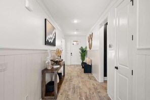 A hallway with a wooden floor, white walls, a door at the end, and a bench with decorative items. - Beach & Lake | Private Pool | Game Room | Near 30A (Panama City Beach)