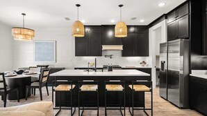 A modern kitchen with a central island, dark cabinetry, stainless steel appliances, and pendant lighting. - Beach & Lake | Private Pool | Game Room | Near 30A (Panama City Beach)