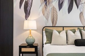 Ein ordentlich gemachtes Bett mit Kissen, einer Nachttischlampe und einer Wand mit Blättermotiv.