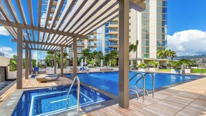 A rooftop pool area with a clear view of a high-rise building, lounge chairs, and palm trees. - Luxury Sky Ala Moana Condo with Ocean & City Views (Honolulu)