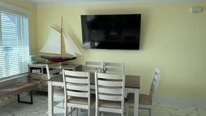 Uma área de refeições com mesa e cadeiras, um modelo de veleiro e uma televisão na parede.