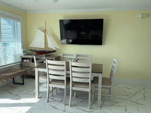 A dining area with a table and chairs, a sailboat model, and a television on the wall. - Come and enjoy your vacation at Bare Feet Retreat in Sands of Laguna (Panama City Beach)