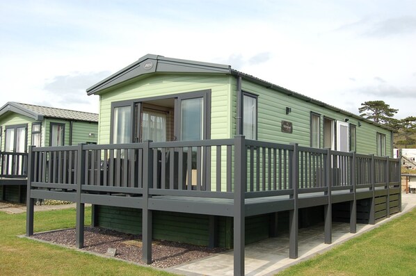 A green mobile home with a balcony and a fenced deck.