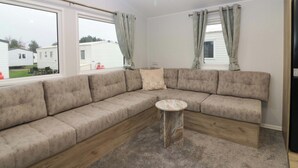 A modern living room with a beige sectional sofa, a small round side table, and large windows with curtains. - 63 St Andrews (Prestonpans)