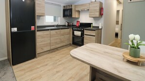 A modern kitchen with wooden cabinets, a black refrigerator, a microwave, and a stove. - 63 St Andrews (Prestonpans)