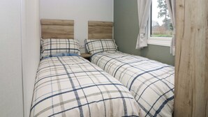 A bedroom with two beds, each with a wooden headboard and matching bedding. - 63 St Andrews (Prestonpans)
