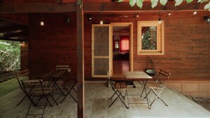 Una cabaña de madera con un patio que incluye mesas y sillas plegables, una puerta de madera y luces de cadena.