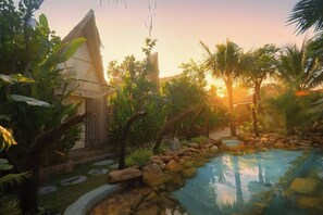 A serene outdoor area with a pool, surrounded by lush greenery and a thatched-roof structure. - LIA Retreat Ba Na Hills (Da Nang)