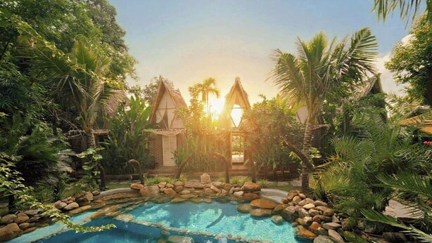 A pool surrounded by rocks and tropical vegetation, with a building in the background. - LIA Retreat Ba Na Hills (Da Nang)