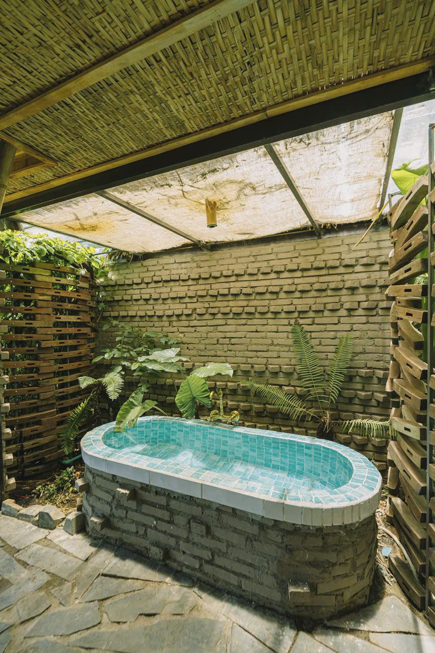 A hot tub with a brick exterior, surrounded by a wooden fence and lush greenery.