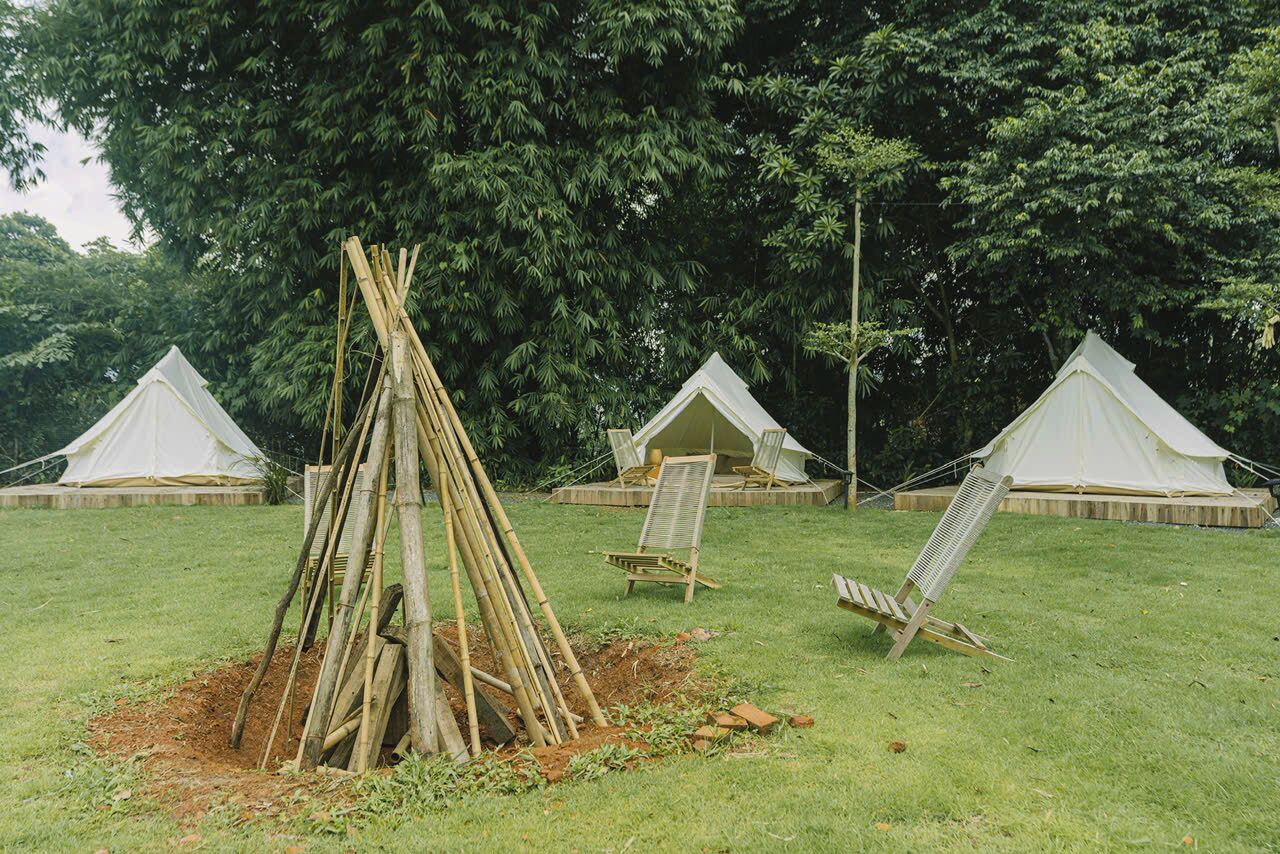 A campsite with three white tents, a central bamboo structure, and two wooden chairs.