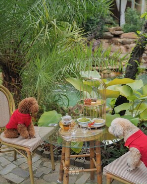 A glass table set outdoors with a tiered stand holding snacks and drinks, surrounded by lush greenery. - LIA Retreat Ba Na Hills (Da Nang)