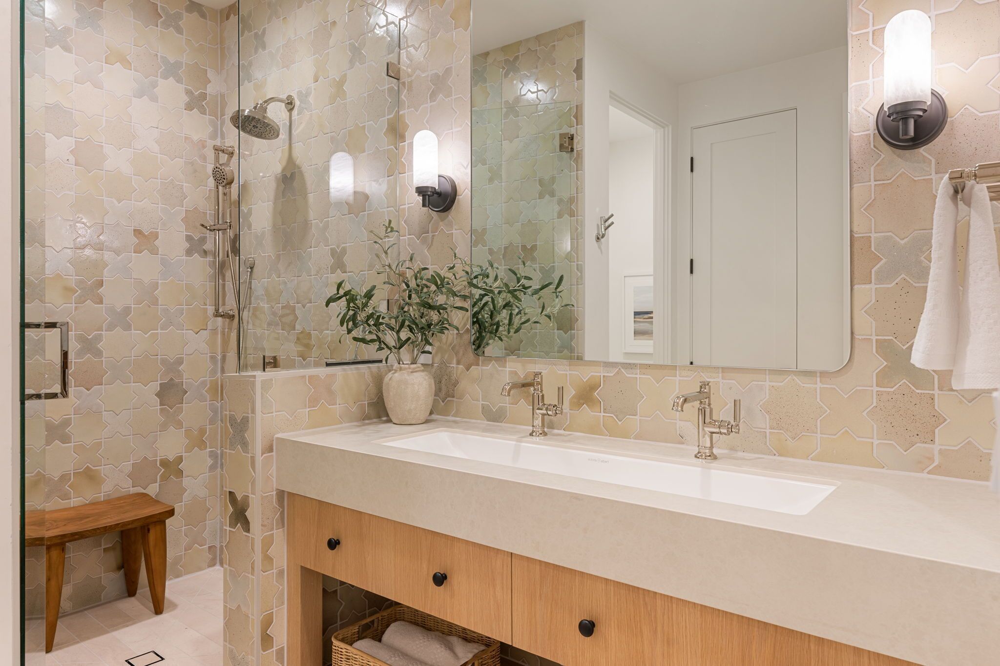 A bathroom with a large sink, a mirror, a shower, and a potted plant.