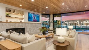 A modern living room with a fireplace, comfortable seating, a television, and a large window with a city view. - The Oasis Utah: Lagoon-Front, Pool, Slide, Theater (St. George)