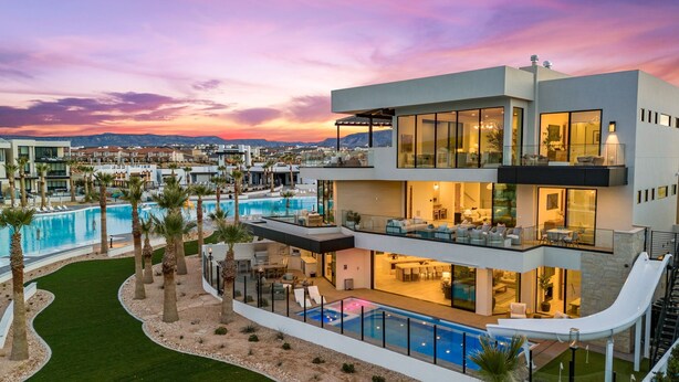 A modern multi-story building with a pool, outdoor seating, and a view of the surrounding area. - The Oasis Utah: Lagoon-Front, Pool, Slide, Theater (St. George)