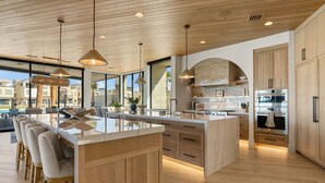 A modern kitchen with wooden cabinets, a central island, and pendant lighting. - The Oasis Utah: Lagoon-Front, Pool, Slide, Theater (St. George)
