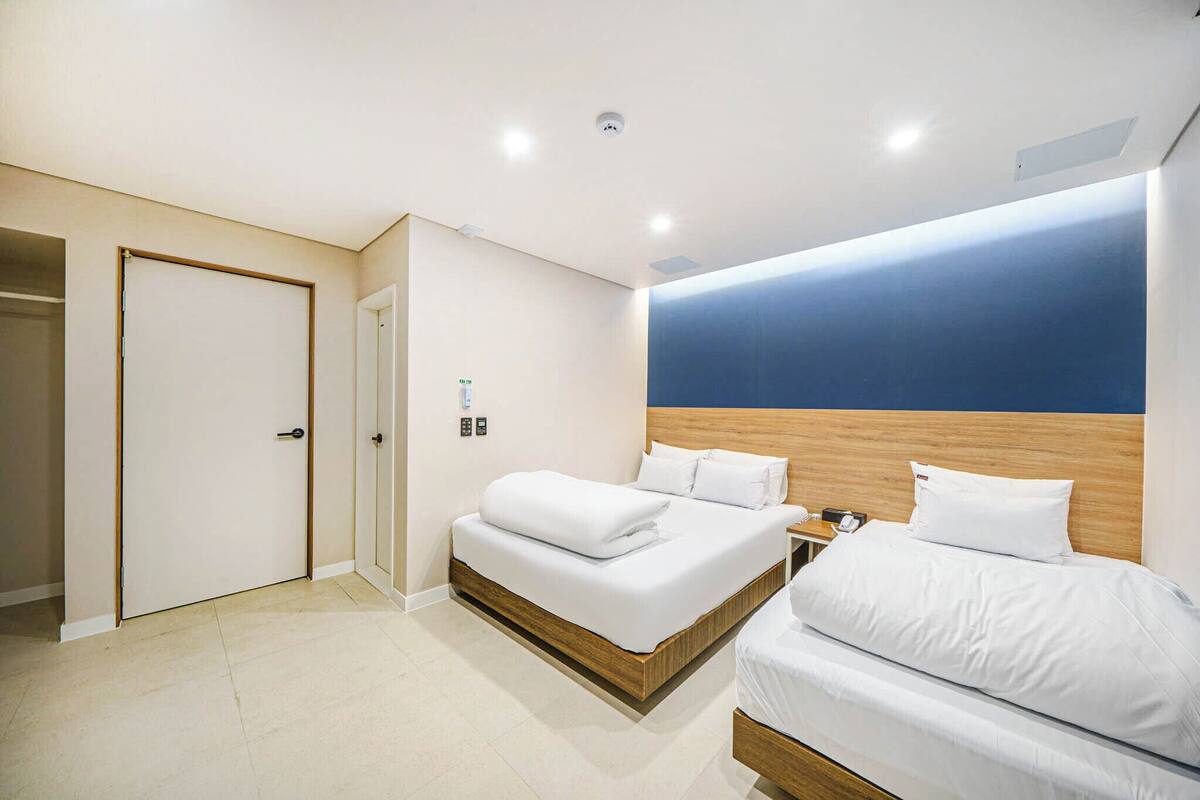 Ein modernes Hotelzimmer mit zwei Betten, einem Holzkopfende, einem großen Fenster und einer Tür.