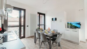 A modern dining area with a table set for four, a television mounted on the wall, and a kitchen area with cabinets and a microwave. - Lake Como Retreat - Menaggio (Menaggio)