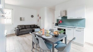A modern kitchen with white cabinets, a dining table with chairs, and a grey sofa in a bright living area. - Lake Como Retreat - Menaggio (Menaggio)