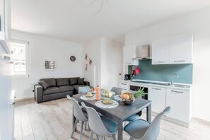 A modern kitchen with white cabinets, a dining table with chairs, and a grey sofa in a bright living area. - Lake Como Retreat - Menaggio (Menaggio)