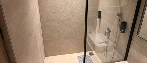 A modern bathroom with a glass-enclosed shower, a white sink, and a marble countertop.
