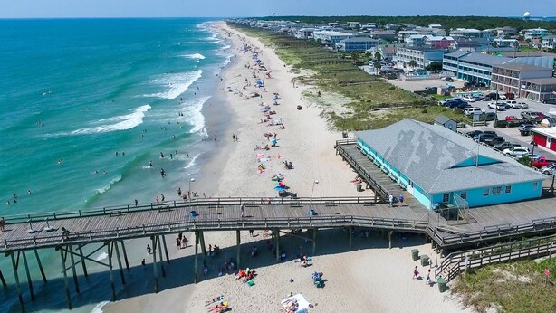 Une plage avec une jetée, des parasols et un bâtiment bleu avec une enseigne.
