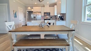 Une cuisine moderne avec des meubles blancs, des appareils en acier inoxydable et une table à manger en bois, accompagnée de bancs.