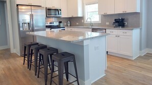 Une cuisine moderne avec des meubles blancs, des appareils en acier inoxydable et un grand îlot central doté de tabourets.