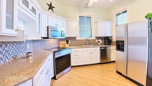 Una cocina moderna con armarios blancos, encimera de granito, refrigerador de acero inoxidable y ventilador de techo.