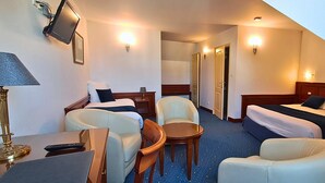 Ett hotellrum med två sängar, ett skrivbord med en lampa, en stol och ett litet bord.