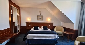 Una camera d'albergo con un letto, una sedia, una scrivania e uno specchio.