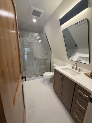 A modern bathroom with a glass shower enclosure, a white toilet, and wooden cabinets.