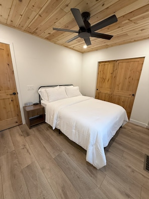 Un dormitorio con cama, suelo de madera, ventilador de techo y puerta de madera.