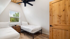A bedroom with a sloped ceiling, a bed, a bedside table, a window with blinds, and a wooden door. - Luxe Forest A-Frame Escape w/ Deck & Fire-Pit (Heber-Overgaard)