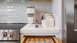 A modern kitchen with a Keurig coffee maker, white mugs, and a drawer with coffee pods. - Luxe Forest A-Frame Escape w/ Deck & Fire-Pit (Heber-Overgaard)