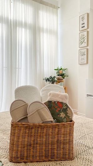 A wicker chair with cushions, a woven rug, a potted plant, and framed botanical prints on the wall. - Zozy Gladstone (London)