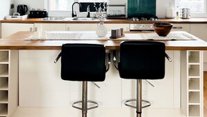 A modern kitchen with a central island, two bar stools, and a view of the city through large windows. - Zozy Gladstone (London)