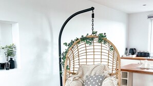 A cozy room with a hanging chair, wooden dresser, and a kitchen area. - Zozy Gladstone (London)