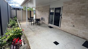 Een overdekt terras met een betonnen vloer, een bakstenen muur, een schuifpui en een kleine tafel met stoelen.