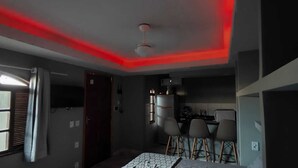 A compact room with a bed, a small kitchenette, and a dining area with bar stools. - Complete Studio 2 (Rio das Ostras)